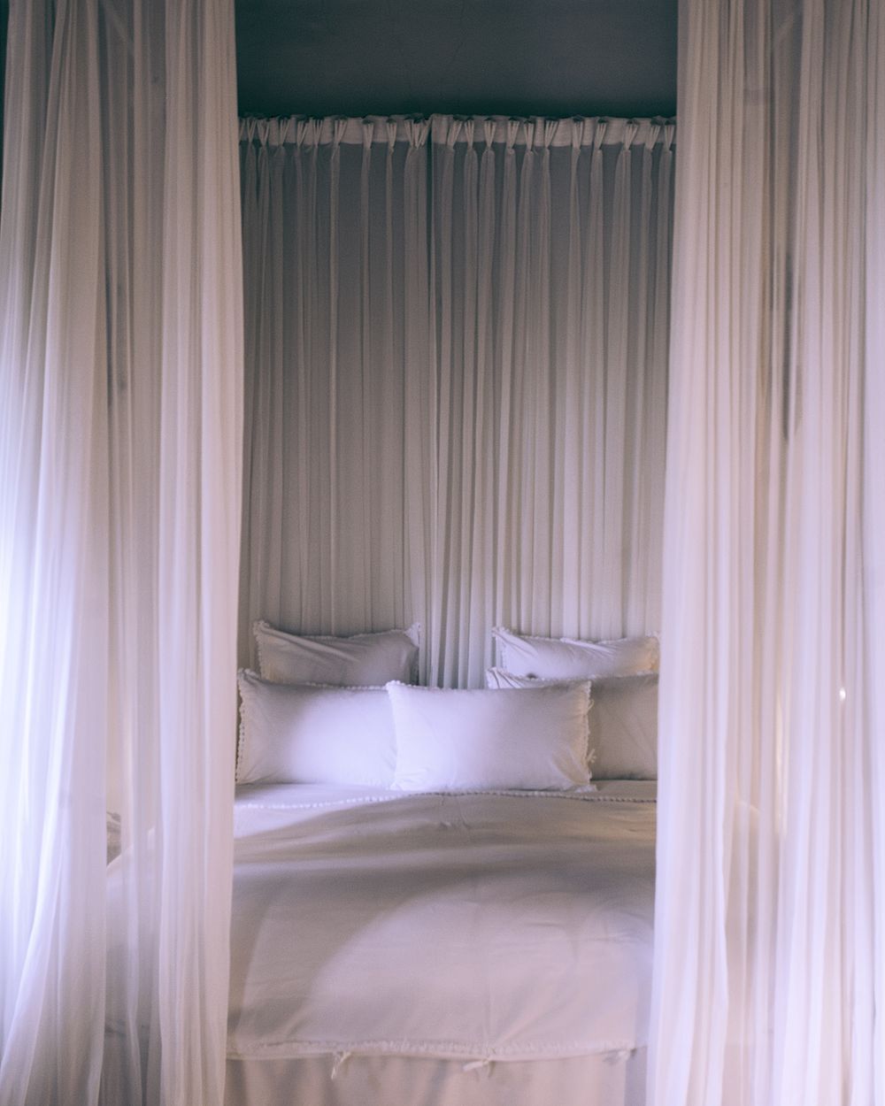 A canopy bed dressed in white linen and woven throws